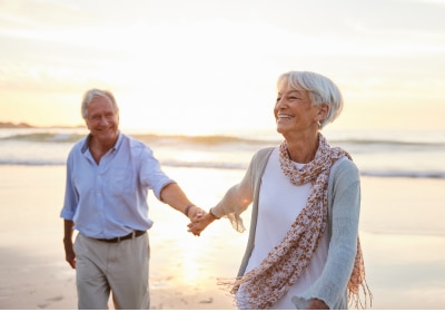Älteres Paar hält Händchen beim Spaziergang am Strand.