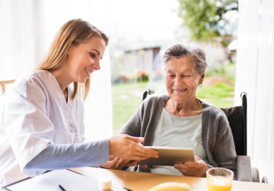 Pflegekraft zeigt älterer Person ein Tablet.