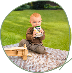Kind sitzt auf einer Picknickdecke im Gras und trinkt aus einem Nestlé Compleat Quetschbeutel.