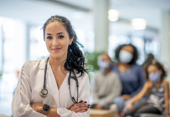 Ärztin mit Stethoskop vor wartenden Patienten im Hintergrund